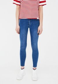 Vaqueros ajustados azul índigo combinados con camiseta de rayas rojas y blancas. El modelo lleva zapatos blancos sin cordones con calcetines tobilleros estampados.