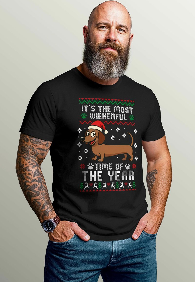 Black T-shirt featuring a graphic design with a cartoon dachshund wearing a Santa hat, text in white and red, festive motifs, and colorful accents.