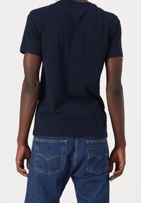 Granatowy bawełniany t-shirt z krótkimi rękawami i standardowym, okrągłym dekoltem, noszony z niebieskimi dżinsami z dwoma tylnymi kieszeniami.