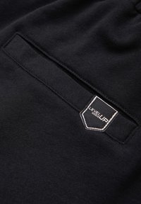 Gros plan sur un tissu noir montrant une poche cousue avec un patch de marque noir et blanc « LEVEL UP » à l'extérieur.