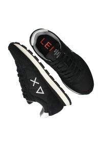 Ein Paar schwarze Laufschuhe mit weißer Sohle, geometrischem Logo an der Seite und rotem Text im Inneren eines Schuhs, der "Läuft schneller als du kannst" liest.