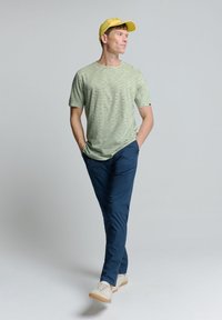 Gestreept groen t-shirt, marineblauwe broek, beige schoenen en een gele pet. De outfit heeft een casual, ontspannen pasvorm en standaard texturen.