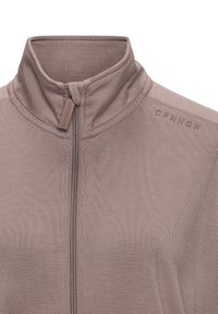 Light taupe zip-up jacket with a high collar, textured fabric, and a subtle logo detail on the shoulder. Features a central zipper closure.