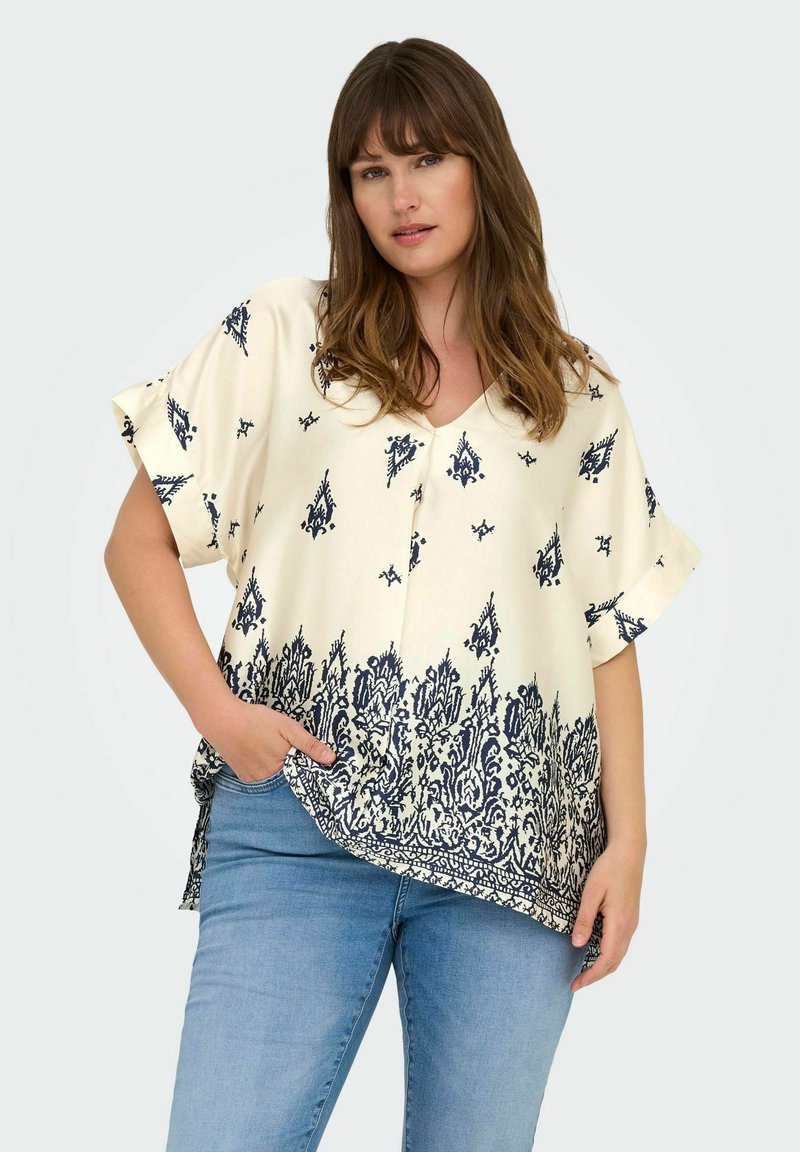 Blusa crema a maniche corte con motivo floreale navy, scollatura a V e tasche laterali; presenta una vestibilità ampia e un orlo curvo.