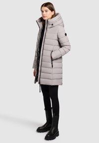 Light gray puffer coat with horizontal stitching, a high collar, and zippered pockets. Paired with black leggings and chunky black boots.
