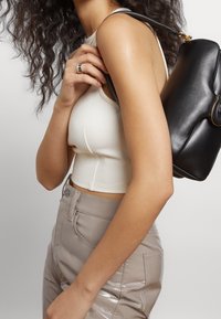 Dopasowany kremowy crop top z okrągłym dekoltem; błyszczące, beżowe spodnie z wysokim stanem; czarna torebka o zaokrąglonym kształcie z złotymi akcentami.