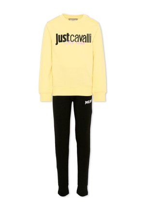 Żółta bluza z długim rękawem z nadrukiem "Just Cavalli" w zestawie z czarnymi spodniami dresowymi z mniejszym logo "Just Cavalli" na udzie.