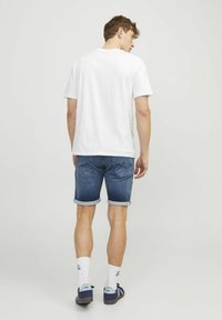 T-shirt bianca a maniche corte con scollo rotondo, abbinata a pantaloncini di denim blu con risvolti e tasche posteriori.