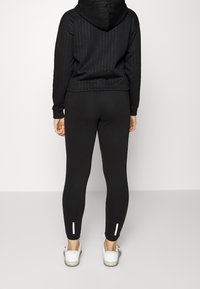 Black hoodie with textured pattern and a kangaroo pocket, paired with black leggings featuring reflective accents at the ankles.