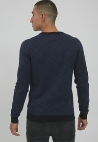 Navy knitted sweater with diamond pattern, crew neck, black ribbed cuffs and hem, form-fitting design, soft texture.