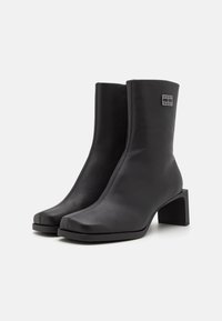 Black leather ankle boots with a square toe and block heel, featuring a side zipper and a small logo plate on the outer side.