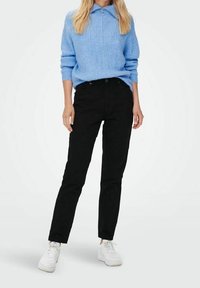 Suéter de canalé color azul claro con cuello y detalle de cremallera frontal, combinado con jeans ajustados negros y zapatillas blancas.