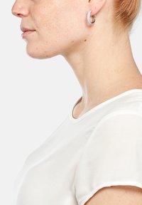 Pendientes de aro con un acabado plateado brillante, adornados con pequeñas piedras preciosas transparentes, exhibidos sobre un fondo neutro.