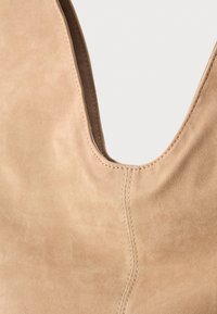 Beige ruskindssko med et dybt V-cut design, der har syede detaljer langs sømmen for ekstra tekstur og form.