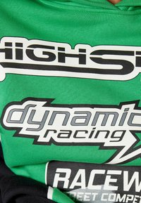 Grüner Baumwoll-Hoodie mit auffälligem schwarz-weiß Grafiktext, auf dem "Highs" und "dynamisches Rennen" deutlich hervorgehoben sind. Glatte Textur, lässiges Design.