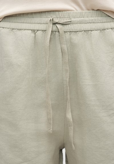 Μπεζ φόρμα με ελαστική μέση και δέσιμο κορδονιού, που δείχνει μέρος ενός μπεζ πουκαμίσου πάνω από τη μέση.