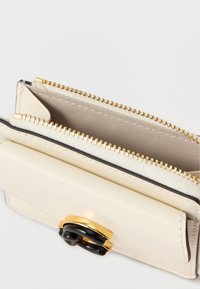 Kermanvärinen nahkalompakko, jossa on kullanvärinen metallilukko ja musta koristus. Vetoketjullisia osastoja ja sileä sisävuori.