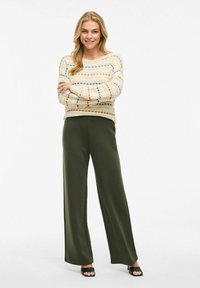 Lätt, krämfärgad stickad tröja med randiga mönster, kombinerad med lösa olivgröna byxor. Svarta sandaler avslutar outfiten.