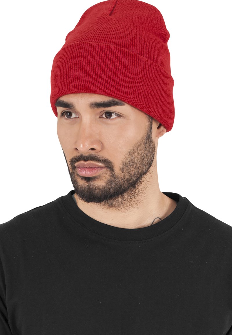 Rød strikket hue med en foldet kant og detaljer ved sømmen på toppen, båret sammen med en sort t-shirt, der viser ribbet tekstur og tætsiddende pasform.