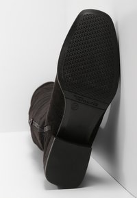 Schwarze Wildleder-Stiefelette mit einer strukturierten Gummisohle, seitlichem Reißverschluss und einem niedrigen Blockabsatz, der auf der Sohle geprägt ist.