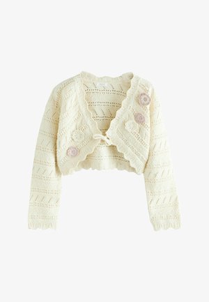 Krótki, kremowy kardigan na szydełku z falistymi krawędziami, wiązany z przodu i ozdobiony trzema pastelowymi aplikacjami kwiatowymi po jednej stronie.