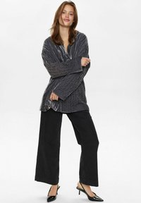 Giacca grigia e texturizzata con scollo a V, abbinata a pantaloni a gamba larga neri con righe sottili e mules nere con tacco.