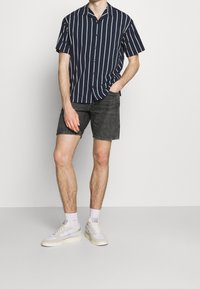 Camisa de manga corta de color navy con rayas verticales blancas, combinada con pantalones cortos gris oscuro y zapatillas blancas. Fondo liso.
