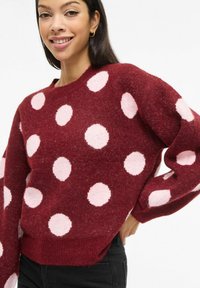 Jersey de punto burdeos con grandes lunares rosas, cuello redondo y dobladillo acanalado. Textura suave con mangas de corte holgado.