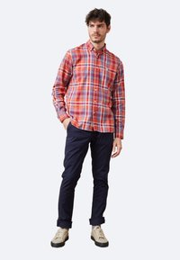 Camisa de cuadros rojos y azules con botones, hecha de algodón, combinada con pantalones azul marino oscuros y zapatillas de color claro.