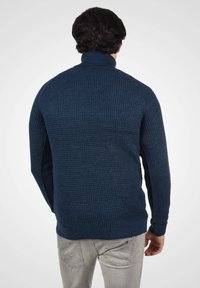 Jūras zilu teksturētu džemperi ar augstu apkakli un ribotām malām. Dizains ir veidots ar austām rakstām un garām piedurknēm.