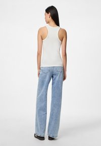 Top sin mangas blanco con canalé y tirantes anchos, combinado con jeans de pierna ancha de color azul claro y zapatos negros. El conjunto presenta un diseño casual.