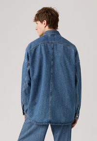 Jeansjakke i mellomblått, med en avslappet passform, spiss krage og knappede ermer. Bak har den en yoke-seam og en rett nederkant.