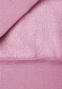 Tejido de color rosa claro que muestra una textura suave, similar al fieltro, en la parte superior y un punto acanalado en la parte inferior, con detalles de costura visibles a lo largo del borde.