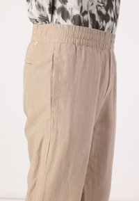 Beige Jogginghose mit elastischem Bund und glatter Textur, ausgestattet mit seitlichen Taschen und dezenten Nähdetails für zusätzliche Struktur.