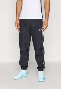 Schwarze Sporthosen mit weißen Seitenstreifen und einem Logo. Getragen mit hellblauen Fußballschuhen mit blauen Akzenten.