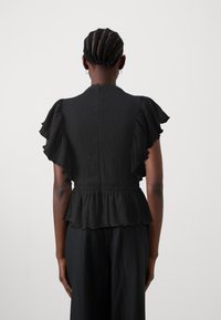 Čierny peplum top s volánovými krátkymi rukávmi a textúrovanou látkou. Má zúžený pás a zapínanie na gombík na zadnej strane.