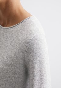 Jasnoszara sweter z szerokim, zaokrąglonym dekoltem i subtelną teksturą. Materiał wydaje się miękki i lekko puszysty.