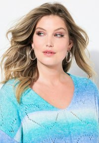 Maglione azzurro chiaro con scollo a V, caratterizzato da una sfumatura che va dal turchese all'azzurro cielo, con dettagli in pizzo. Orecchini a cerchio in argento.