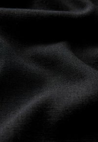 Čierna tkanina s hladkou textúrou, s jemnými variáciami v tkaní. Jemný padavý vzhľad, ktorý zdôrazňuje jednoduchý dizajn bez vzorov.
