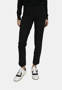 Pantaloni neri a sigaretta realizzati in un tessuto morbido, con fessure laterali alle caviglie, abbinati a sneakers bianche con dettagli neri.