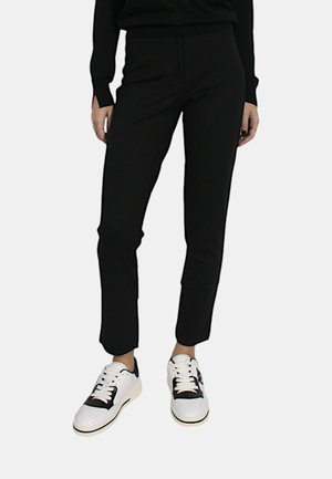 Pantaloni neri a sigaretta realizzati in un tessuto morbido, con fessure laterali alle caviglie, abbinati a sneakers bianche con dettagli neri.