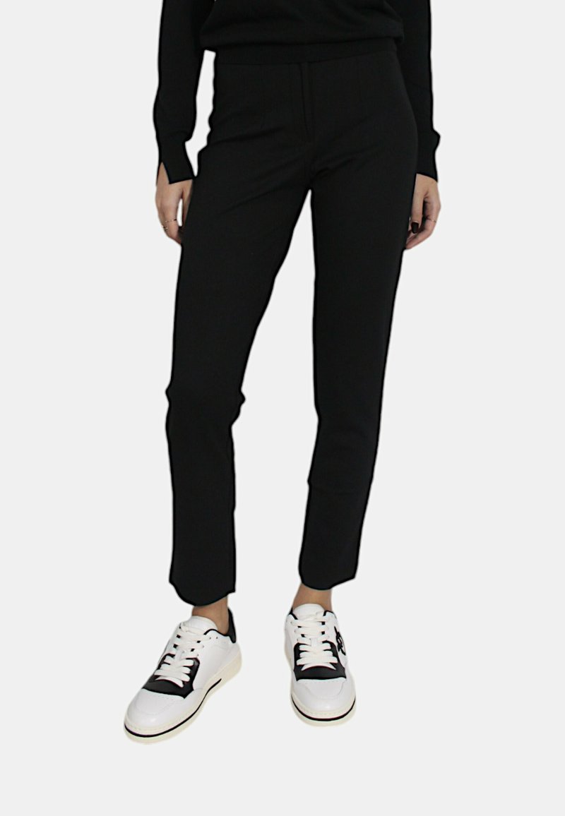 Pantaloni neri a sigaretta realizzati in un tessuto morbido, con fessure laterali alle caviglie, abbinati a sneakers bianche con dettagli neri.