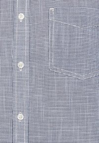 Geweven shirt met een geruit patroon in zwart en wit. Heeft een knoopsluiting aan de voorkant en een linkse borstzak met contrasterende stiksels.