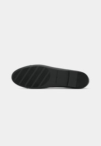 Semelle d'une chaussure habillée noire avec une texture antidérapante et le logo "Tommy Hilfiger" sur un fond blanc.