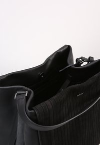 Černá kožená kabelka s ribbenou semišovou texturou. Má strukturovaný tvar, nastavitelný popruh a zacvakávací uzávěr pro bezpečnost.