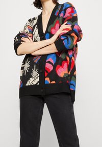 Strickjacke mit schwarzem Grund, die farbenfrohe Blumenmuster in Rosa, Blau und Grün aufweist, abgeschlossen mit einem tiefen V-Ausschnitt und Knopfverschluss.