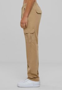Khaki cargo kalhoty s elastickým pasem, bočními kapsami a volným střihem, doplněné o bílé tenisky na neutrálním pozadí.