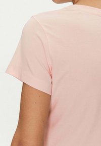 T-shirt rosa a maniche corte con una texture morbida e scollo rotondo. La cucitura è visibile lungo le maniche e l'orlo per un tocco di dettaglio aggiuntivo.