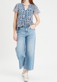 Blue and white patterned blouse with short sleeves, paired with high-waisted light blue wide-leg jeans and beige lace-up sneakers.