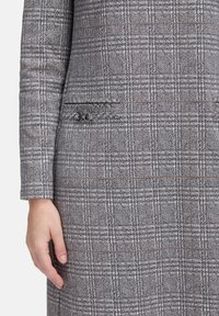 Blazer grigio a quadri con tessuto testurizzato, vestibilità slim, tasca frontale singola con chiusura decorativa e silhouette strutturata.